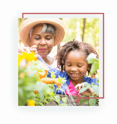 Senior woman in a hat watering plants with smiling young girl